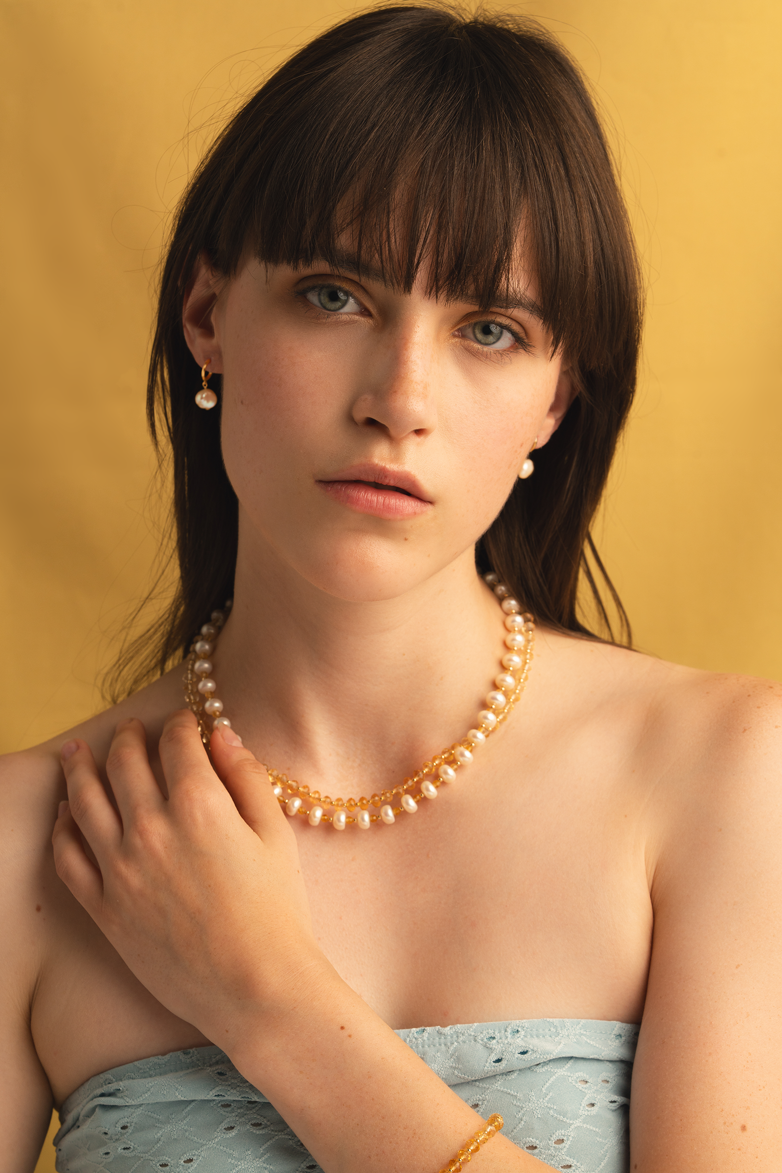 Model wearing handcrafted fine jewelry set featuring a double-strand necklace of freshwater pearls and natural citrine beads, paired with 14k gold and pearl drop earrings. Photographed against a golden background.