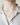 Person wearing small diamond and pearl pendant necklace with gold cable chain, layered under white blouse.